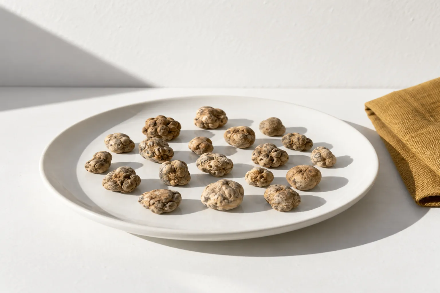 Piccoli sclerozi beige e marroni su un piatto bianco, accanto a un tovagliolo color ocra